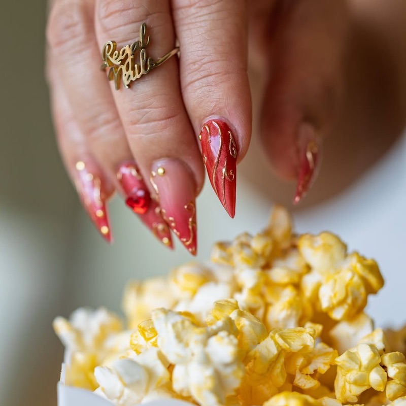 Uñas stiletto rojas con líneas doradas y cristales